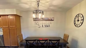 Uma sala de jantar com mesa e cadeiras de madeira, um candelabro, um relógio de parede e uma frase motivacional na parede.
