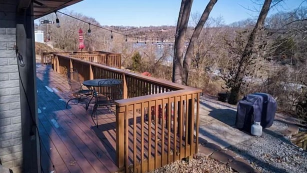 Um deck de madeira com mesa e cadeiras, com vista para um corpo de água e árvores.