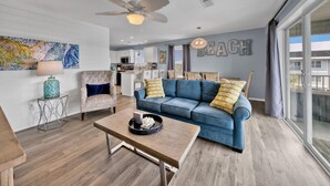 A modern living room with a blue sofa, a wooden coffee table, a pendant light, and a ceiling fan. - Blue Haven- Beachside condo - 4 minute walk to sand! (Santa Rosa Beach)