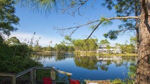 A lakeside deck with chairs and a warning sign, surrounded by trees and a house in the background. - Blue Haven- Beachside condo - 4 minute walk to sand! (Santa Rosa Beach)