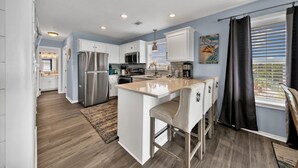 A modern kitchen with a central island, stainless steel appliances, and a bar area with stools. - Blue Haven- Beachside condo - 4 minute walk to sand! (Santa Rosa Beach)