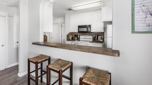 A kitchen with white cabinets, a microwave, a stove, and a bar area with stools.