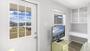 A room with a large window, a television on a cabinet, and a white shelving unit.