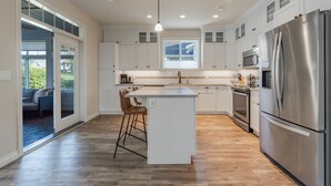 Una cocina moderna con armarios blancos, un refrigerador de acero inoxidable y una isla central con taburetes de bar.