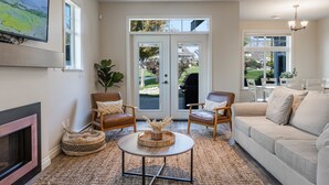 Una sala de estar con chimenea, dos sillones, un sofá, una mesa de centro y un televisor montado en la pared.