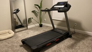 Ein Heimfitnessraum mit Laufband, Spiegel, Blumentopf und Haustierbett.
