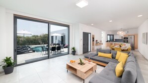 A modern living room with a grey sofa, a wooden coffee table, and a dining area with yellow chairs.