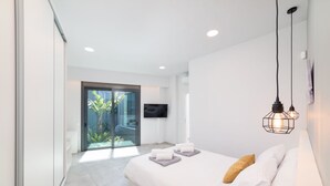 A modern bedroom with a bed, a TV, and a glass door leading to a balcony.