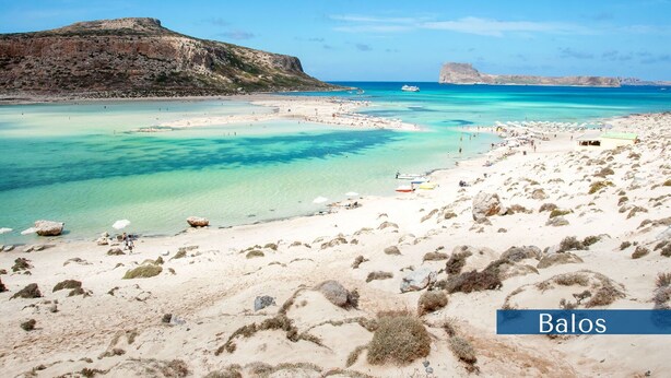 A beach with clear turquoise waters, rocky outcrops, and a distant mountain.