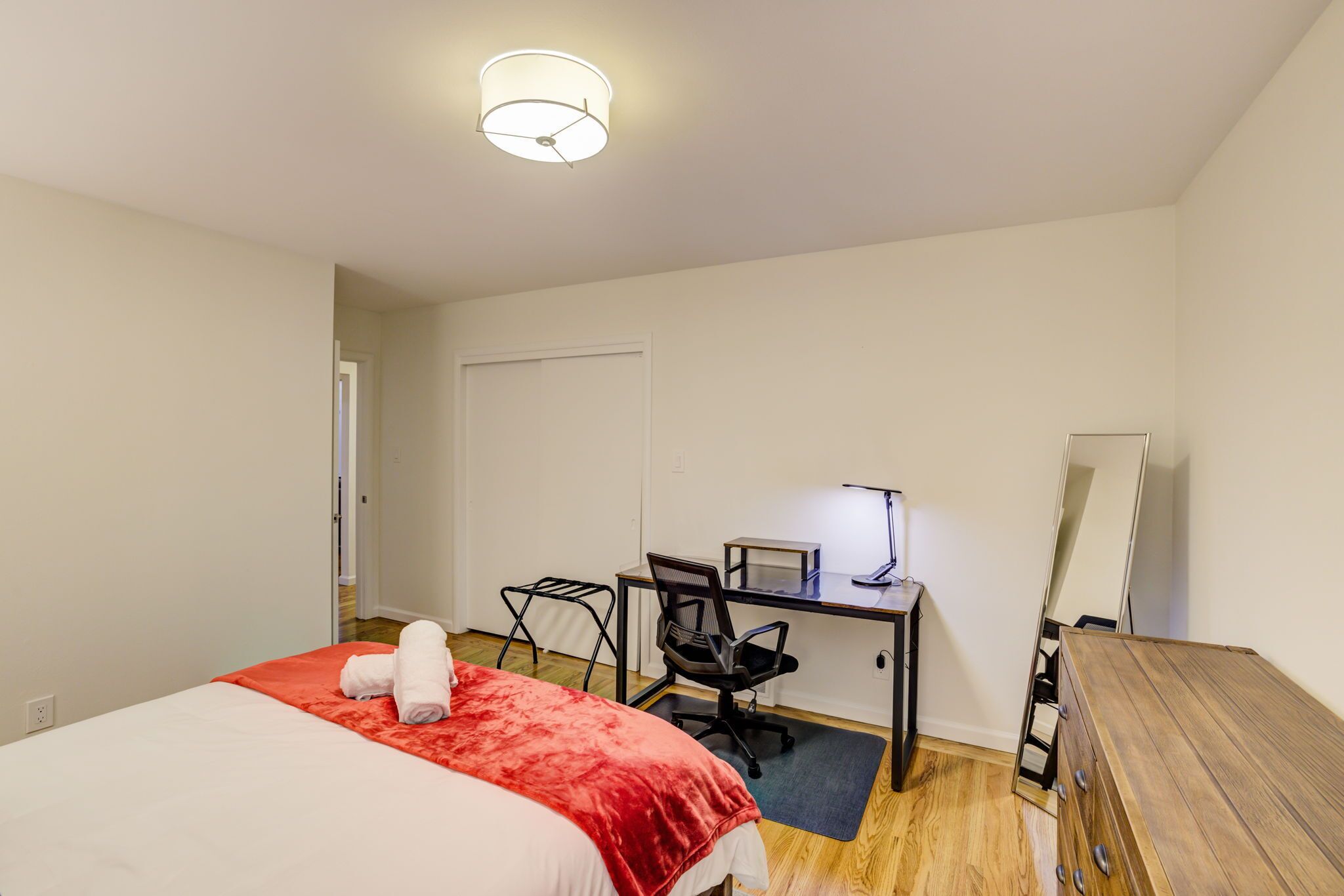 A bedroom with a bed, a desk, a chair, and a mirror.