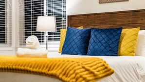 A neatly made bed with a yellow throw blanket, blue and yellow pillows, and a white towel on the side. - RUSTIC/MODERN DESIGN, OASIS CITY GETAWAY/NEAR SFO (South San Francisco)