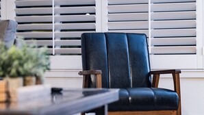 A dark blue leather chair with wooden legs and armrests, positioned in front of a window with white blinds. - RUSTIC/MODERN DESIGN, OASIS CITY GETAWAY/NEAR SFO (South San Francisco)