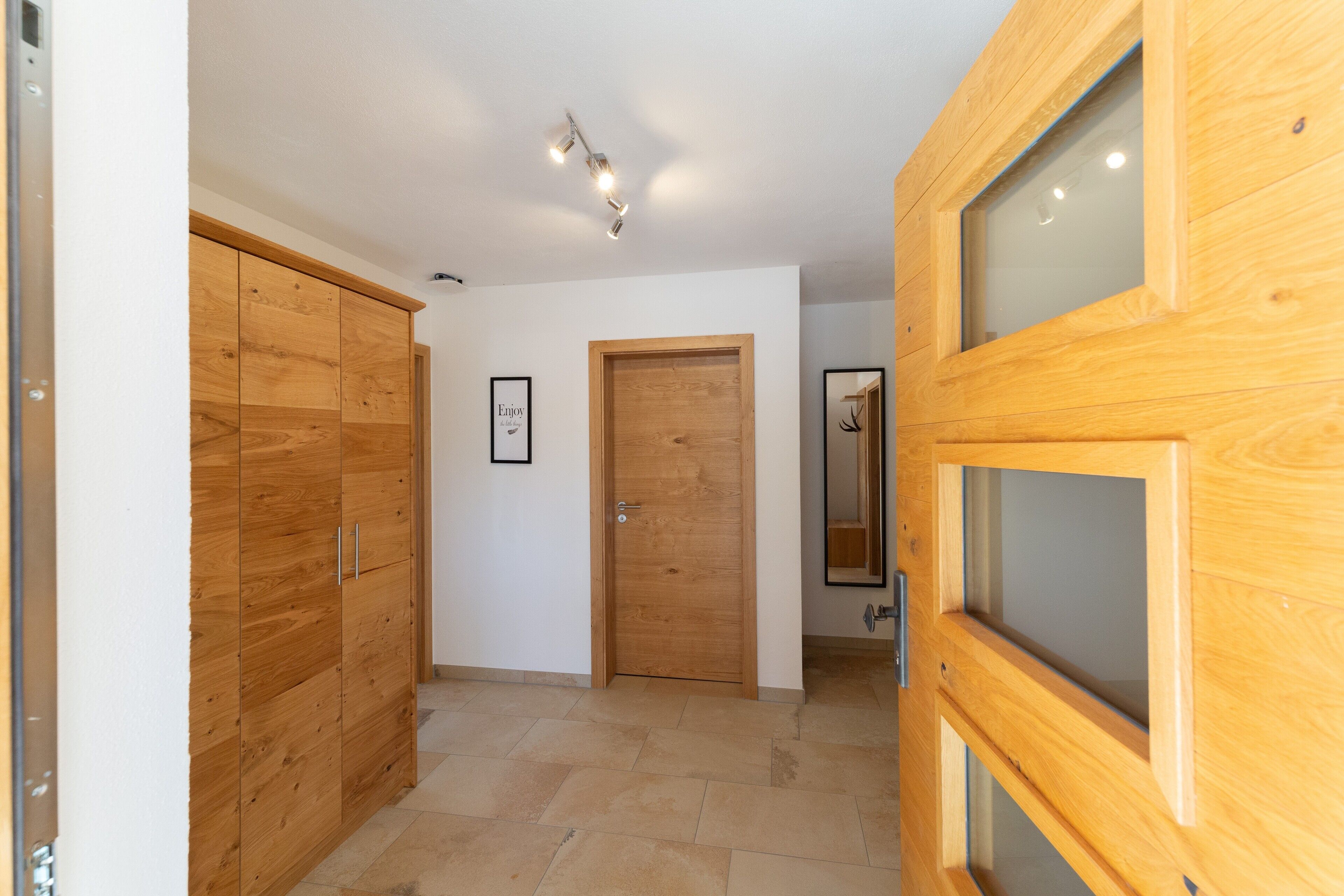 A hallway with wooden wardrobes, a wooden door, and a mirror.