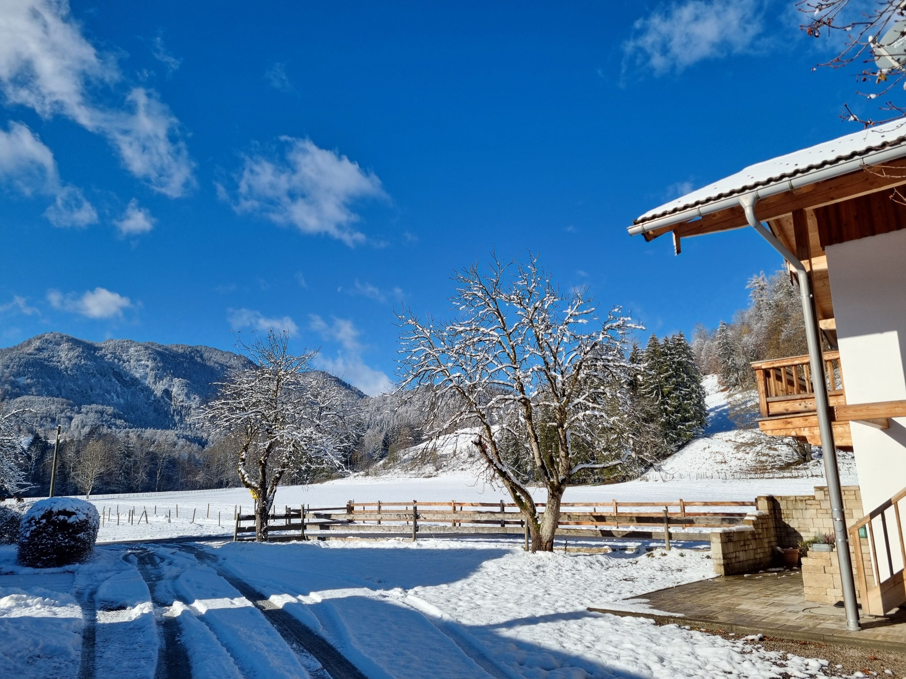 Schneebedeckte Landschaft mit einer Holzhütte, blauem Himmel und Bergen im Hintergrund.