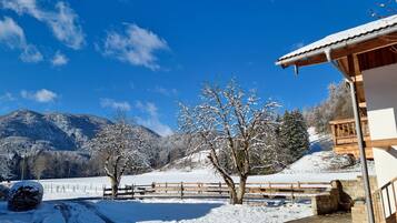 Schneebedeckte Landschaft mit einer Holzhütte, blauem Himmel und Bergen im Hintergrund.