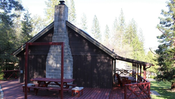 A rustic cabin with a stone chimney, a wooden deck, and a covered porch. - Rustic Chapparal Cabin at Bass Lake Heights (Oakhurst)
