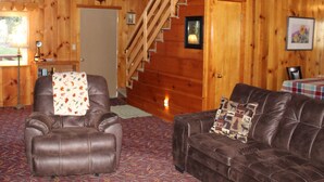 A wooden interior with a leather sofa, a recliner, and a staircase. - Rustic Chapparal Cabin at Bass Lake Heights (Oakhurst)