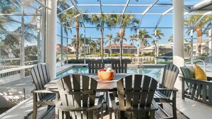 Un espace aménagé au bord de la piscine, avec des fauteuils Adirondack, une table sur laquelle est posé un saladier, et une vue sur les palmiers et les maisons.