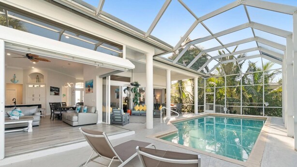 Un vaste espace intérieur abritant une piscine, avec un plafond en verre, un coin repas et un salon doté d’un canapé et de fauteuils.