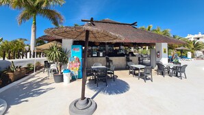 An outdoor seating area with tables and chairs, a thatched-roof structure, and a visible ice cream freezer. - 145 m2 apartment with complex view, bar-restaurant, swimming pools, sea 300 m from the sea (Adeje)