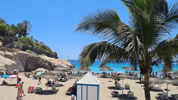 A beach with thatched umbrellas, lounge chairs, and a small building, likely a beach hut. - 145 m2 apartment with complex view, bar-restaurant, swimming pools, sea 300 m from the sea (Adeje)