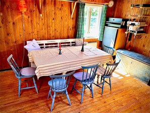 A wooden interior with a dining table, four chairs, a bench, and a kitchenette. - Rosenlund - Holiday cottage Rosenlund (Älmhult)