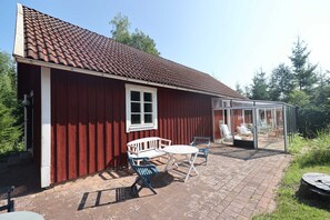 A red building with a tiled roof, a white window, and a glass-enclosed patio area with outdoor furniture. - Rosenlund - Holiday cottage Rosenlund (Älmhult)
