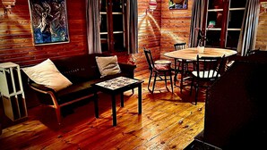 A cozy cabin interior with a wooden floor, a sofa, a dining table with chairs, and a painting on the wall. - Rosenlund - Holiday cottage Rosenlund (Älmhult)