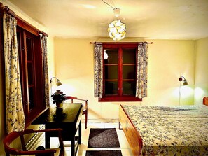 A bedroom with a bed, a desk, a chair, a window with curtains, and a hanging light fixture. - Rosenlund - Holiday cottage Rosenlund (Älmhult)