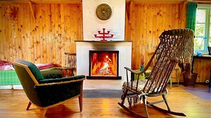 A cozy room with wooden walls, a fireplace, a rocking chair, and a chair with a green cushion. - Rosenlund - Holiday cottage Rosenlund (Älmhult)