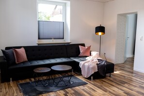 A modern living room with a black sofa, two round wooden tables, a black floor lamp, and a window with blinds. - Beautiful vacation apartment in Oberkotzau am Fichtelgebirge (Oberkotzau)