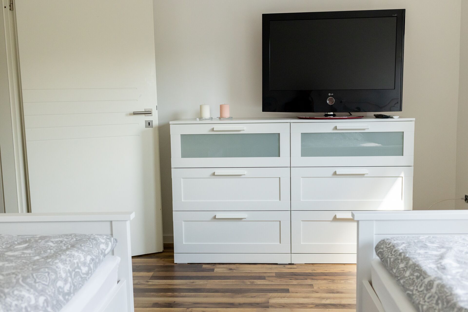 Ein Schlafzimmer mit einer weißen Kommode, einem Flachbildfernseher und zwei Betten mit gemusterten Bettbezügen.