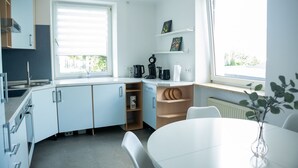 A modern kitchen with white cabinets, a sink, and a window. There is a white dining table with chairs and a vase with a plant.