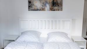 A bedroom with a white bed, two nightstands, and a large abstract painting on the wall.