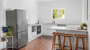 Une cuisine moderne avec des meubles blancs, un réfrigérateur en acier inoxydable, des tabourets de bar en bois et une fenêtre laissant entrer la lumière naturelle.