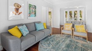 Un salon avec un canapé gris, des coussins jaunes et bleus, un tapis rond et deux œuvres d’art encadrées accrochées au mur.