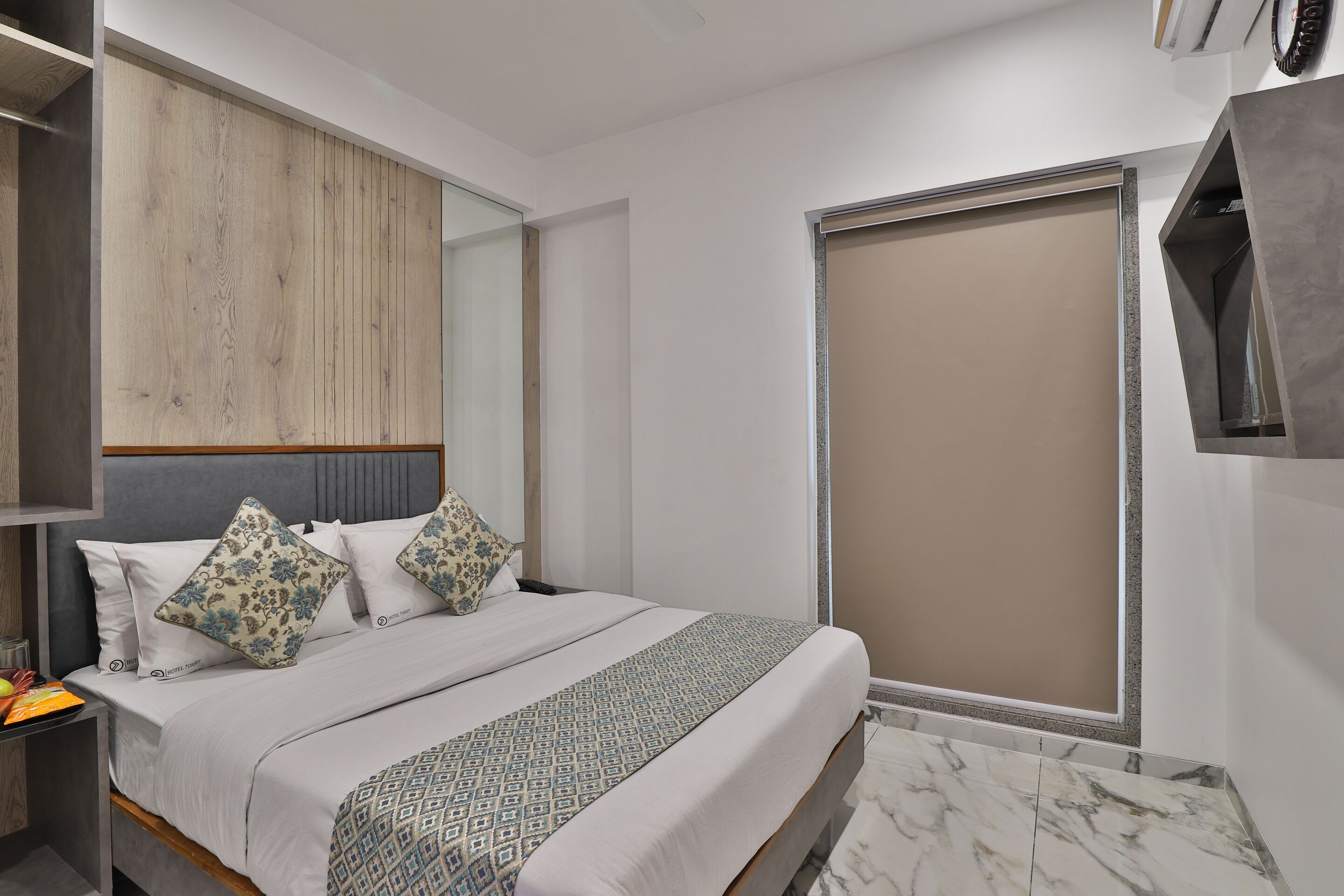 Une chambre moderne comprenant un lit, une table de chevet, une armoire et une grande fenêtre avec un store.