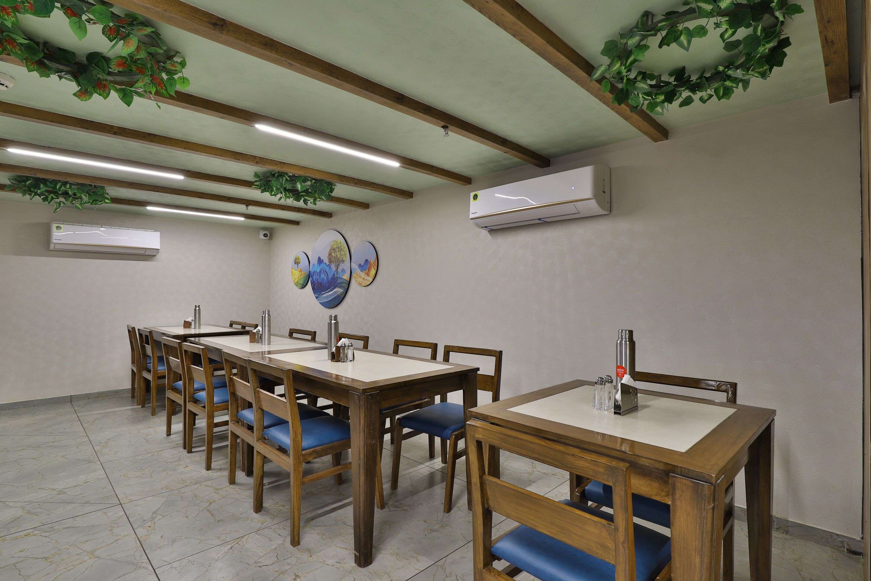 A dining area with wooden tables and chairs, ceiling beams, and wall-mounted air conditioning units.