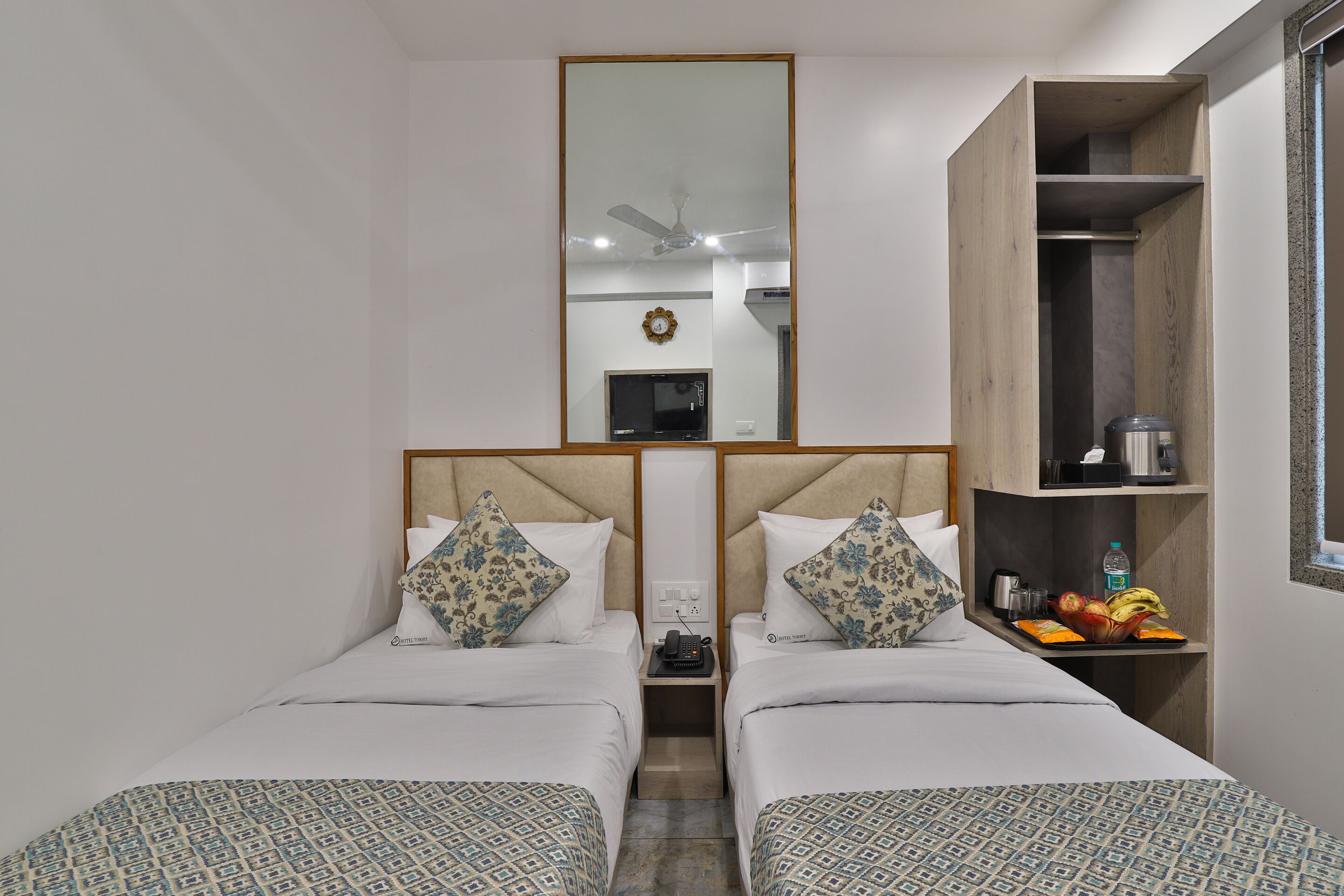 A hotel room with two beds, a mirror, a wardrobe, and a small table with a fruit tray.