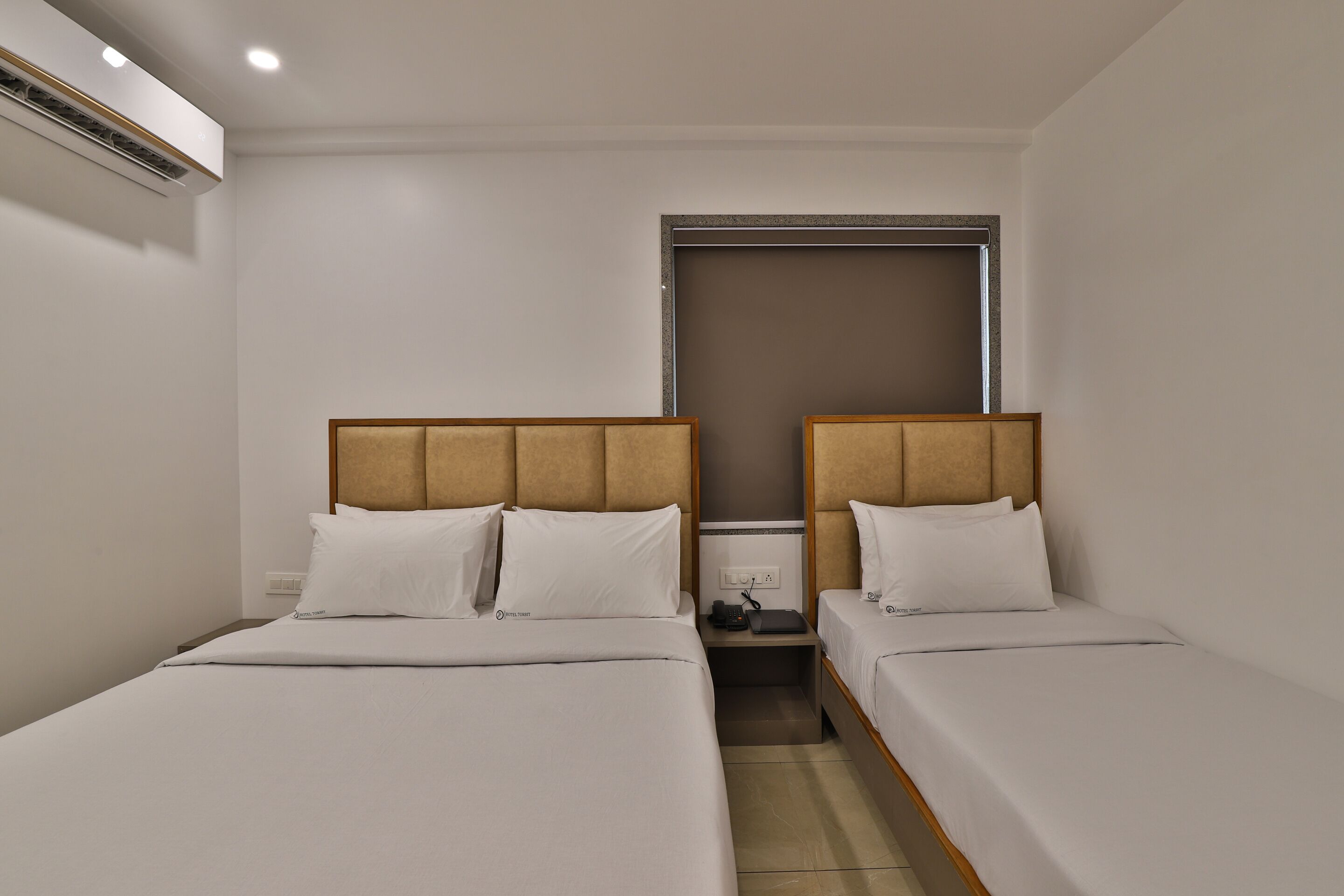 Ein Hotelzimmer mit zwei Einzelbetten, einem kleinen Nachttisch, einem Beistelltisch und einem Fenster mit Blick.