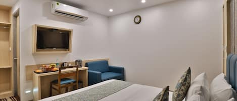 Habitación de hotel con cama, escritorio con silla, televisión, equipo de aire acondicionado y un reloj en la pared.
