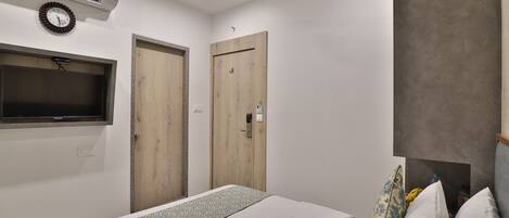 Une chambre à coucher avec un lit, un téléviseur fixé au mur, deux portes en bois et un ventilateur de plafond.