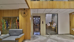 Um lobby moderno com um sofá cinzento, uma parede de madeira e área de elevadores.