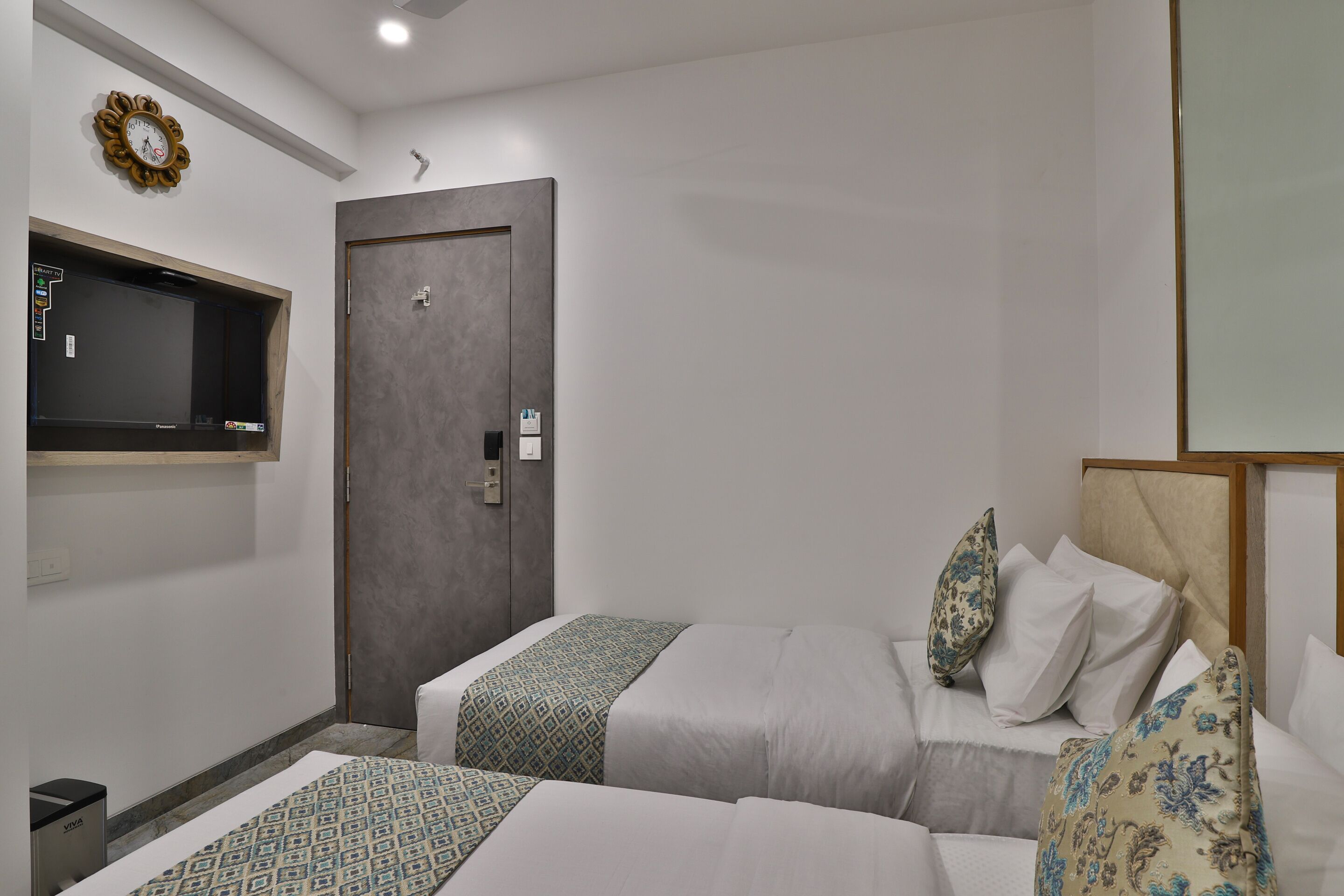 A hotel room with two beds, a wardrobe, a TV mounted on the wall, and a small trash bin.