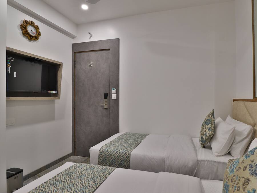 A hotel room with two beds, a wardrobe, a TV mounted on the wall, and a small trash bin.