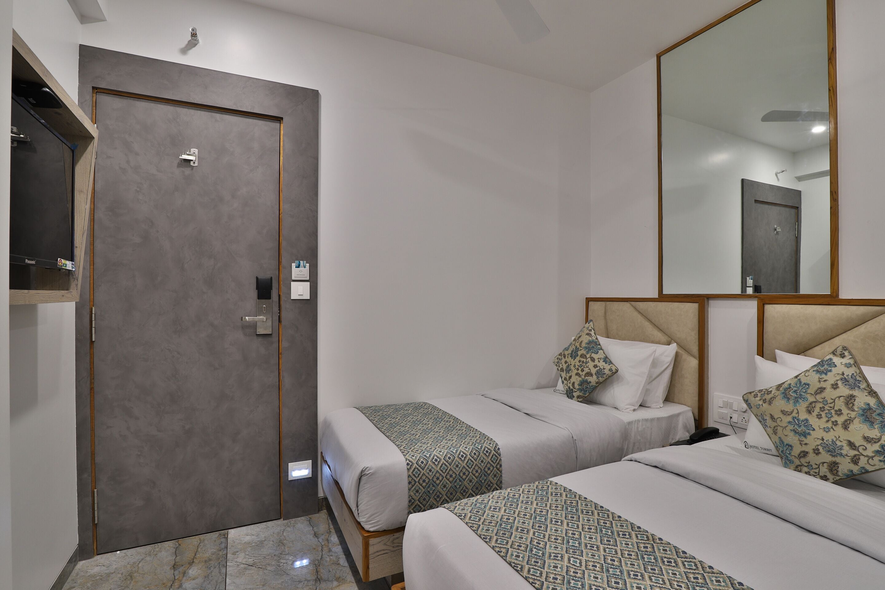 Habitación de hotel con dos camas, un espejo grande, un armario y una puerta.
