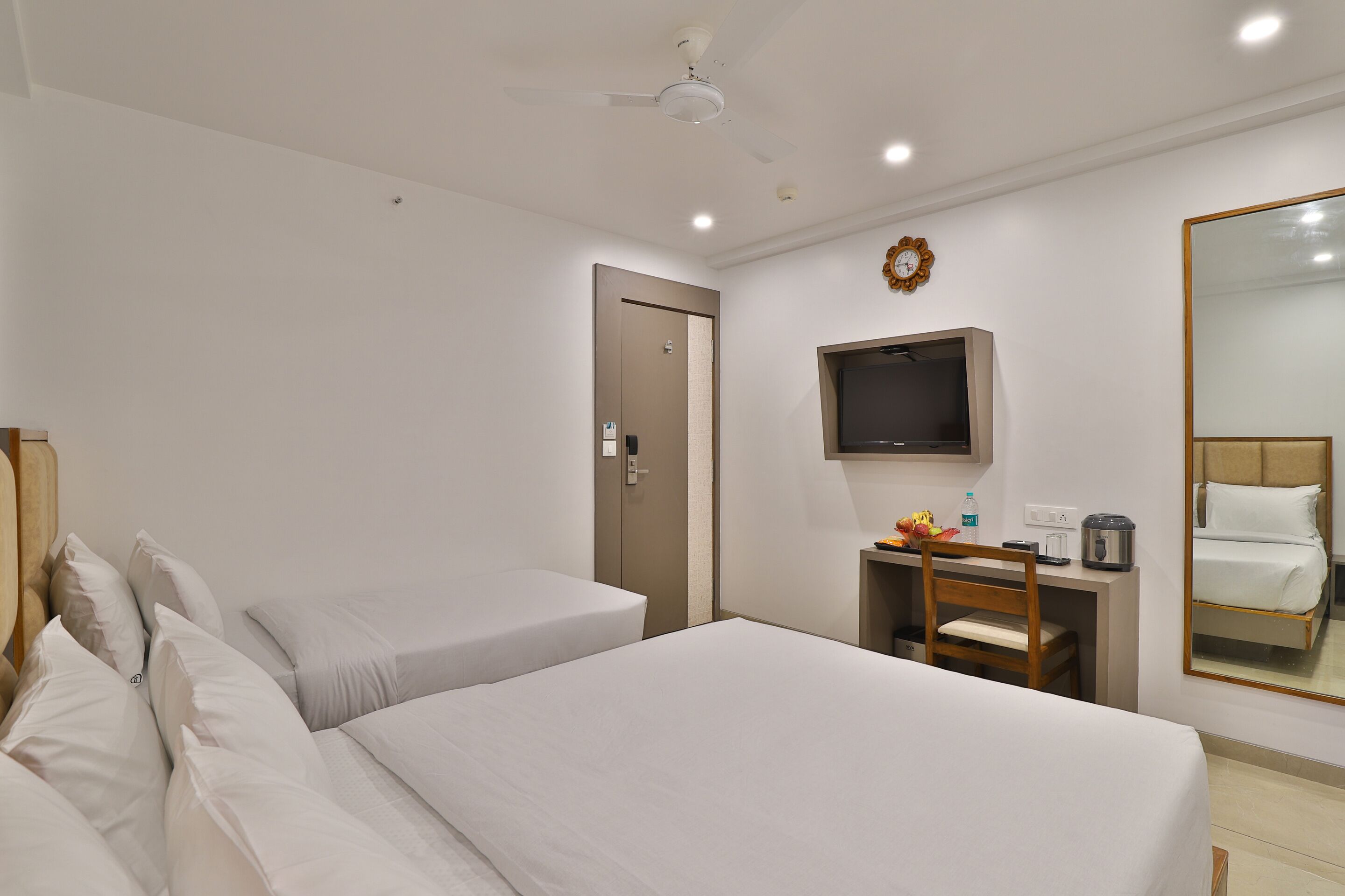 Ein Hotelzimmer mit zwei Betten, einem Schreibtisch mit Stuhl, einem Fernseher und einem Spiegel.