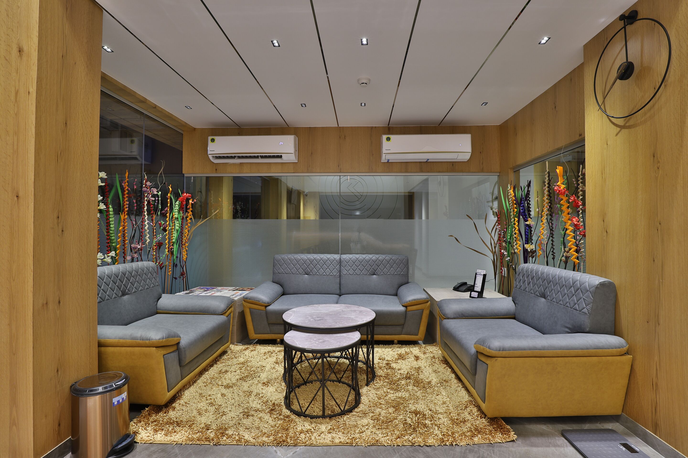 A modern lounge area with a grey sectional sofa, two round tables, and decorative plants.