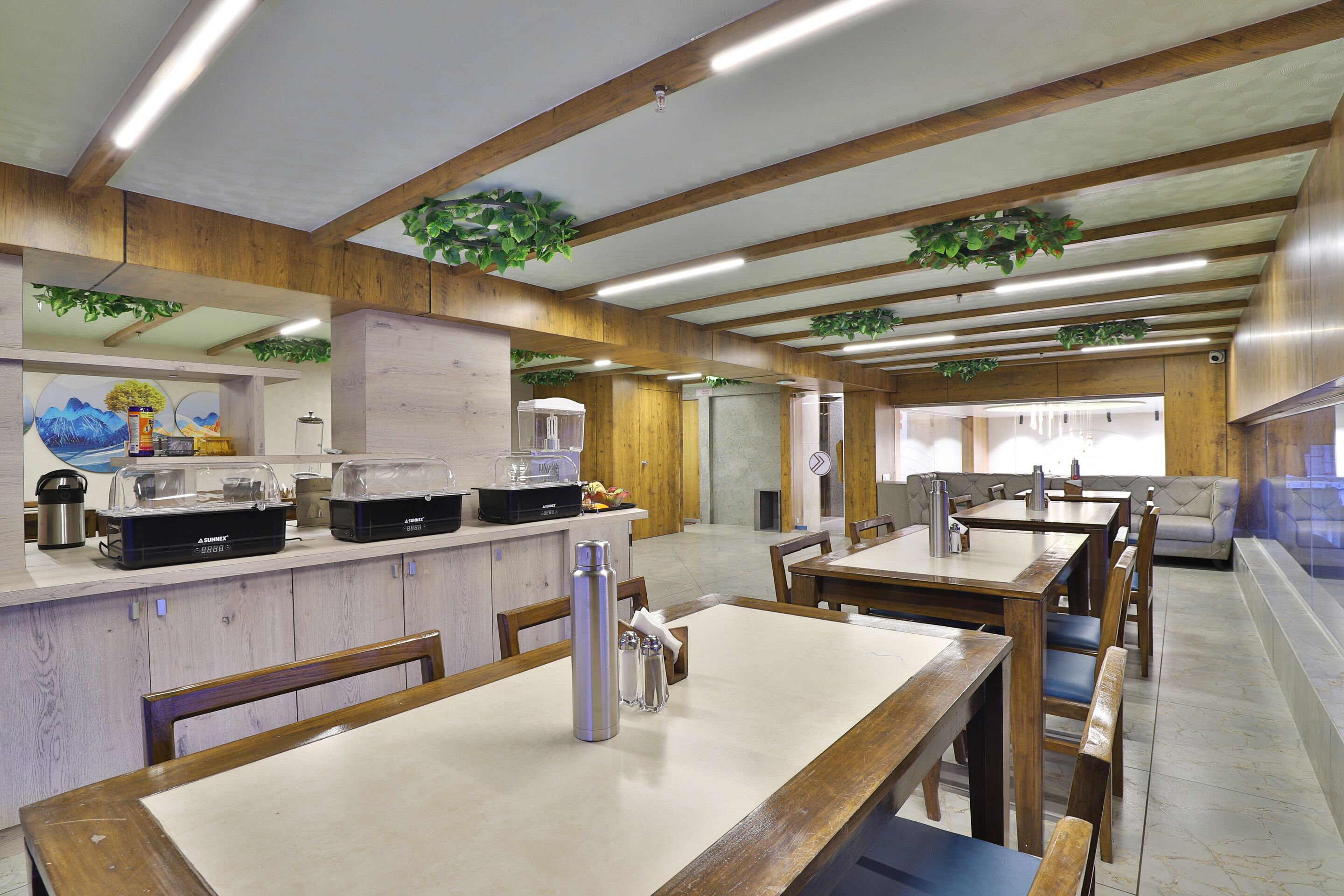 A restaurant with wooden beams, white tables, and green plants on the ceiling.
