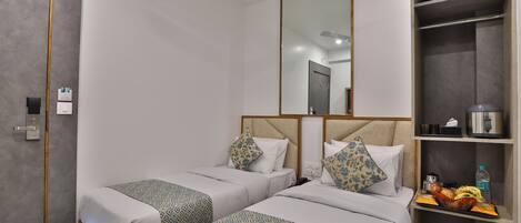 A hotel room with two single beds, a large mirror, a wardrobe, and a tray with fruits and a bottle.